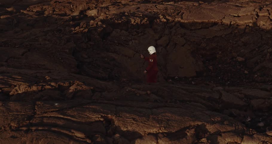 A person in a space suit picks rocks up from the soil and examines them
