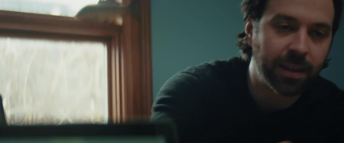 A man is sitting indoors next to a window