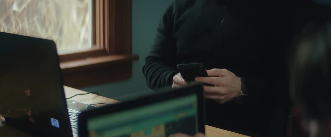 A man is sitting indoors and talking on a cell phone