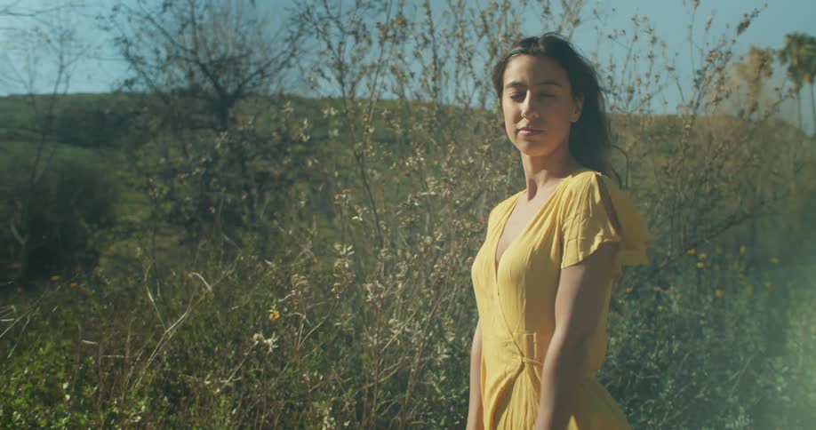 A woman stands at the base of a hill and looks around