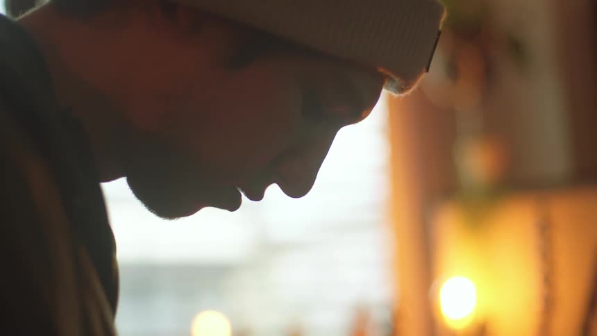 A young man wearing a beanie plays a guitar in a room with other guitars lining the wall