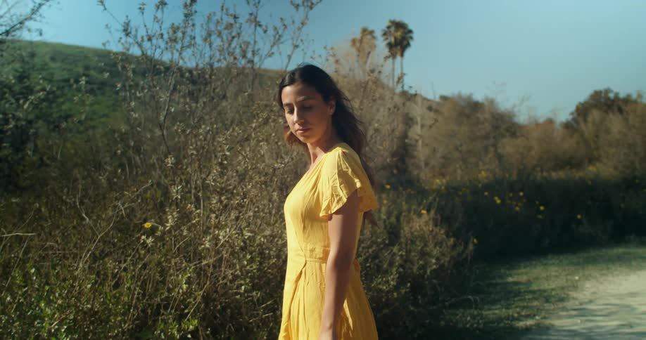 A young woman in a yellow dress stands outdoors and poses for the camera