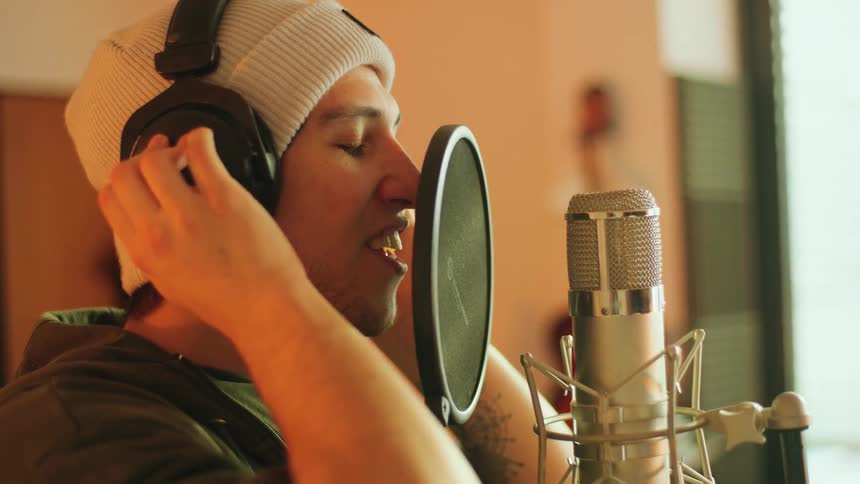 A man in a room with headphones singing into a microphone with a pop guard