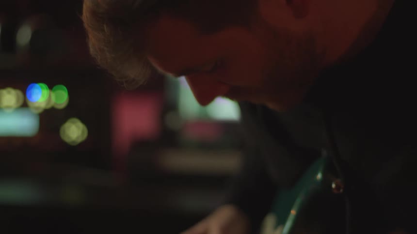 Man bobs his head while playing guitar near multiple computers sitting on table