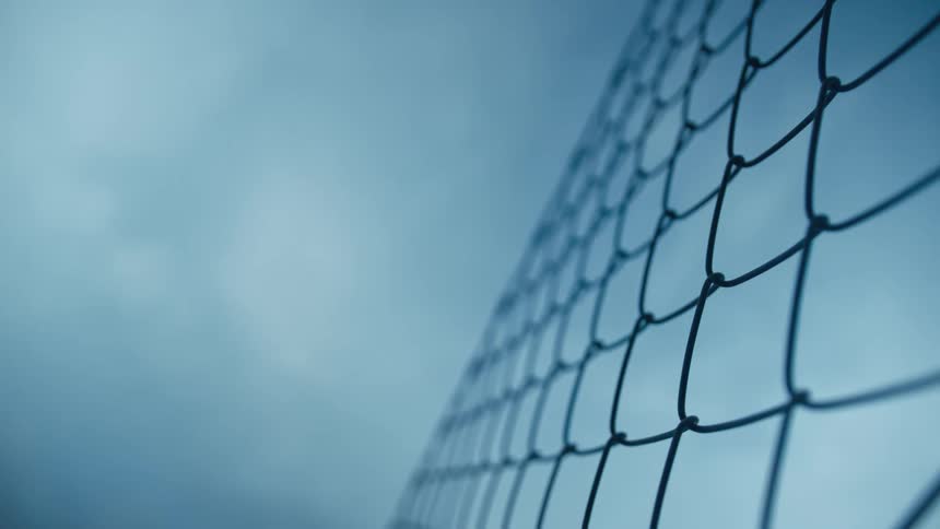 A chain link fence under a cloudy blue sky
