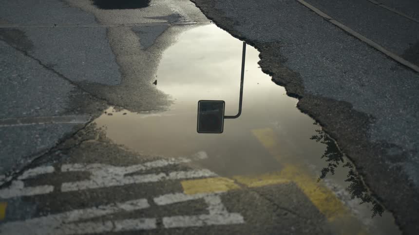 Puddle in asphalt parking lot near lettering and marking reflects sky and streetlight