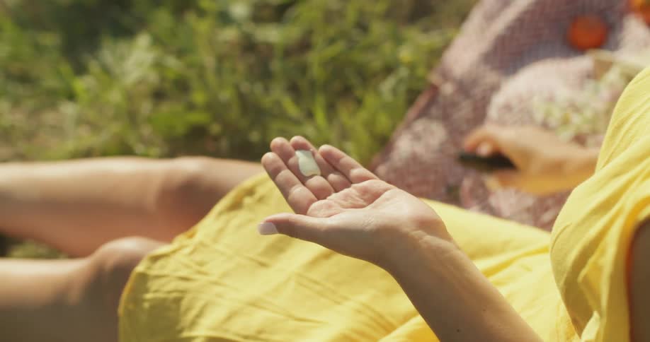 A woman in a yellow dress sitting on a blanket on grass and applying cream to her hands