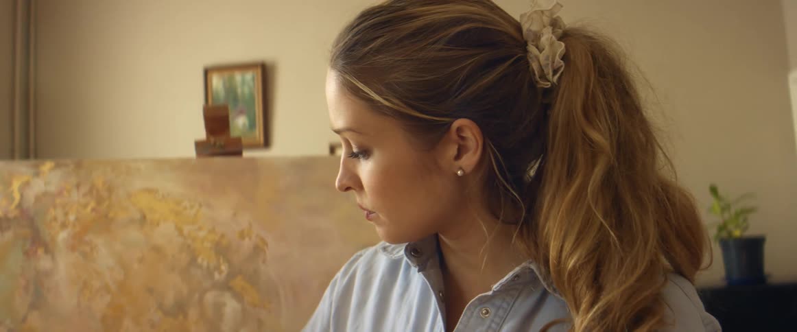 A woman is sitting indoors next to a painting