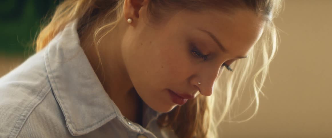 A woman in a room looking downwards with a wall in the background