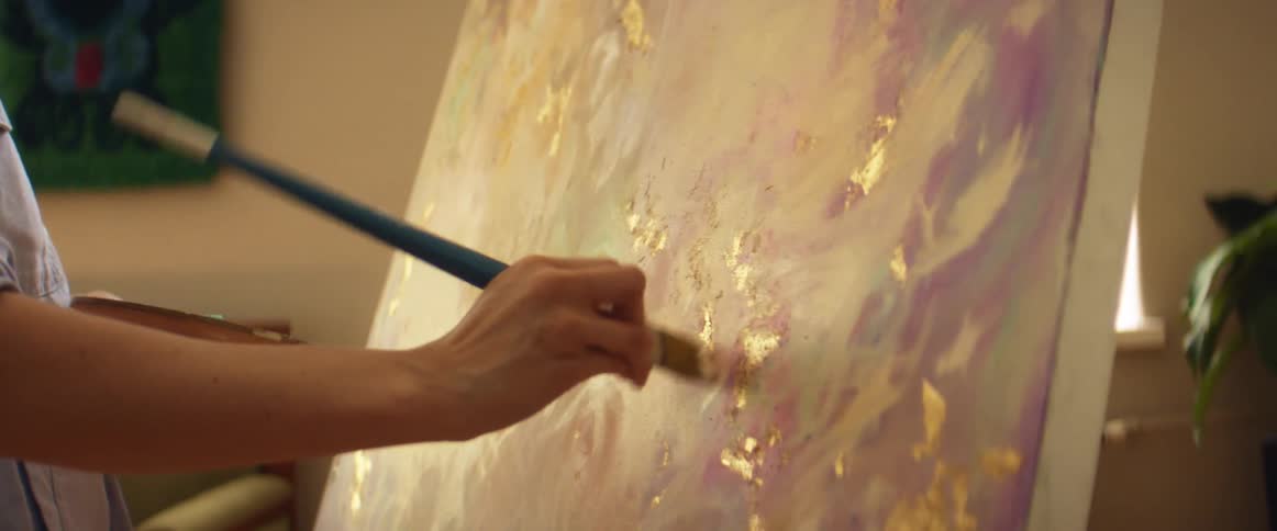 A woman painting with a brush over canvas inside a room