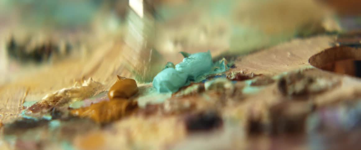 A painter squeezes paint from a small tube onto a wooden palette before dabbing the paint with a brush
