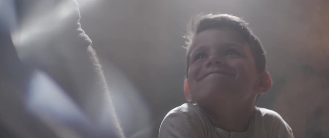A man is working on something on a bench as a boy watches