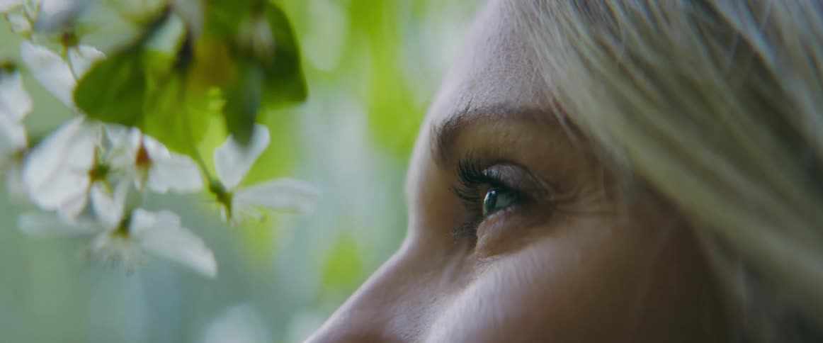 Eye of a blonde woman under the white flowers hanging from a tree