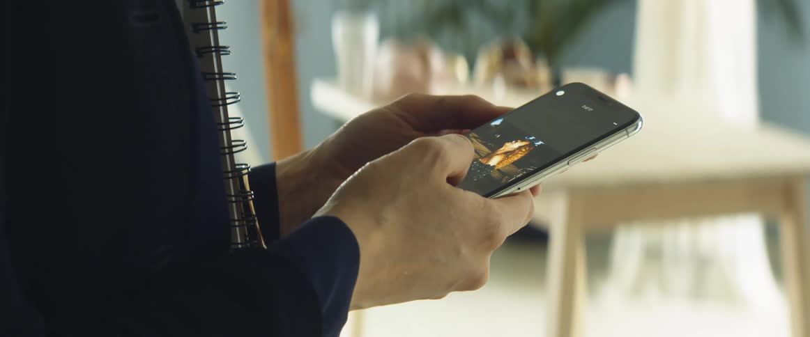 A person uses their thumb to swipe through photographs on a smartphone while standing indoors during the day
