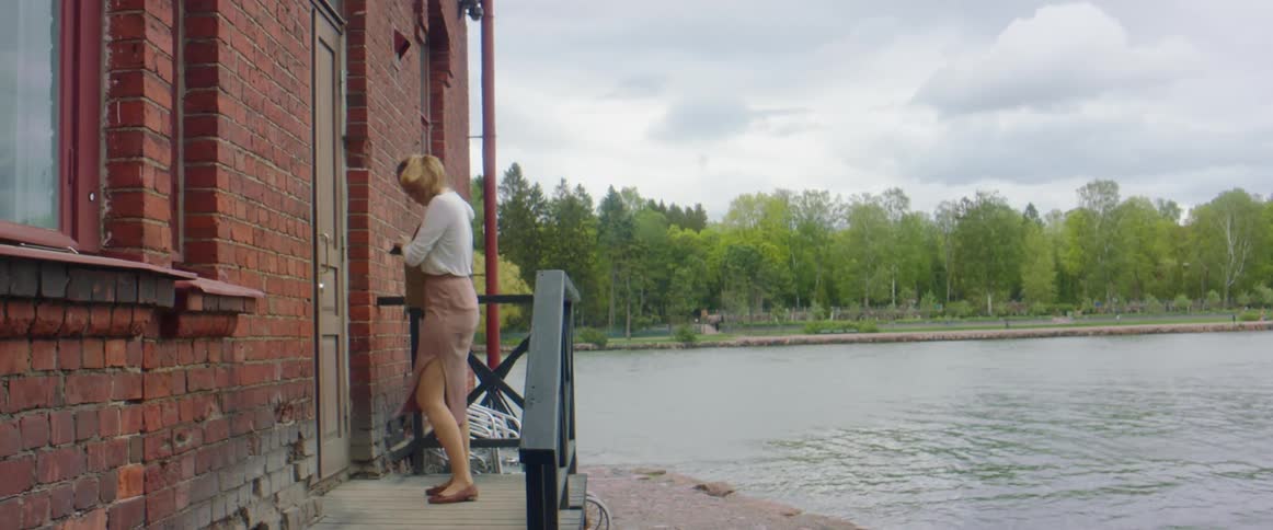 A woman walks to the side entrance of a building beside a lake and takes keys out of her purse