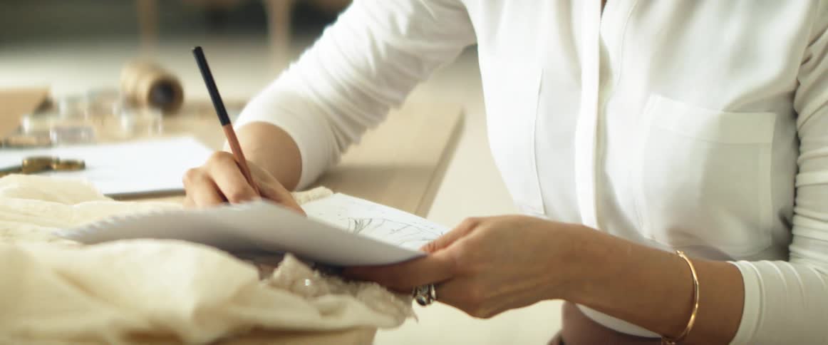 A woman is drawing a design for a dress