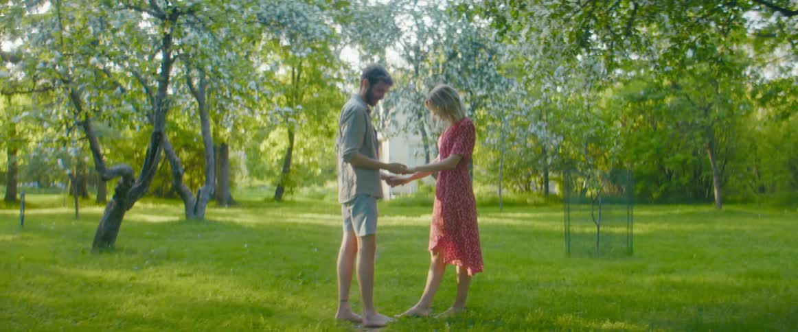 A man and woman kiss one another while standing in a field during the day