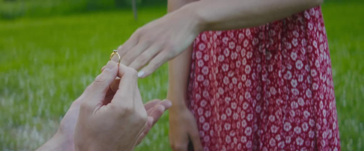 A person kneels and holds a ring out to purpose to the woman standing in front of them