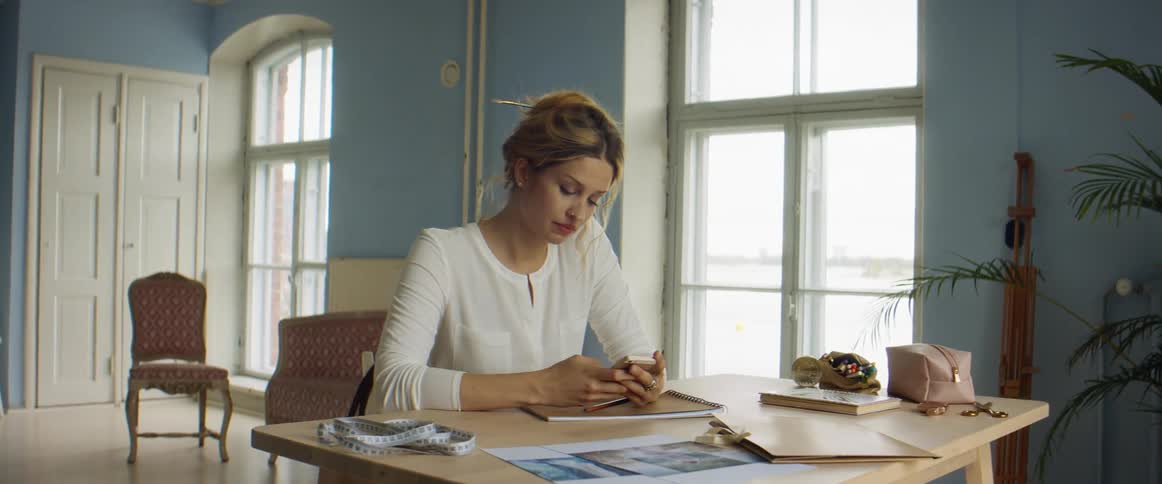 A woman is sitting at a desk and is typing on her phone