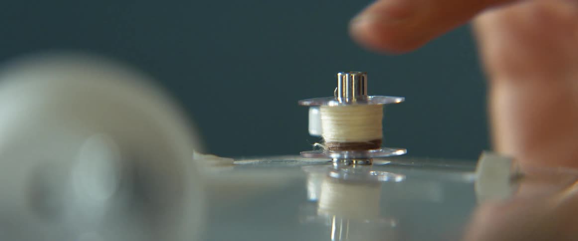 A hand places a bobbin on a sewing machine and then removes it