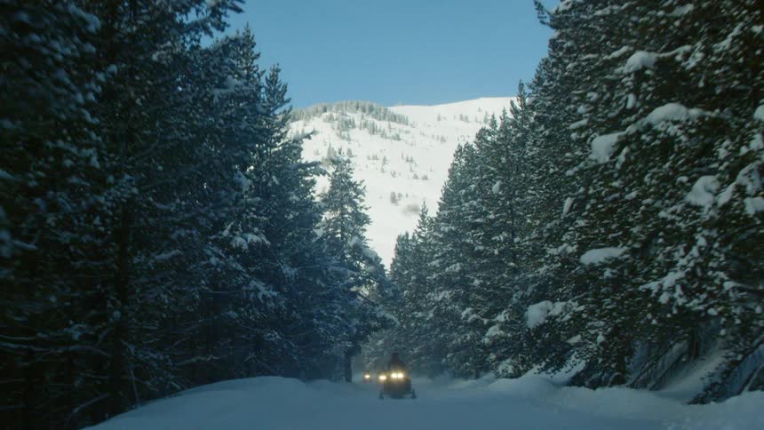 Three people are riding snowmobiles in winter