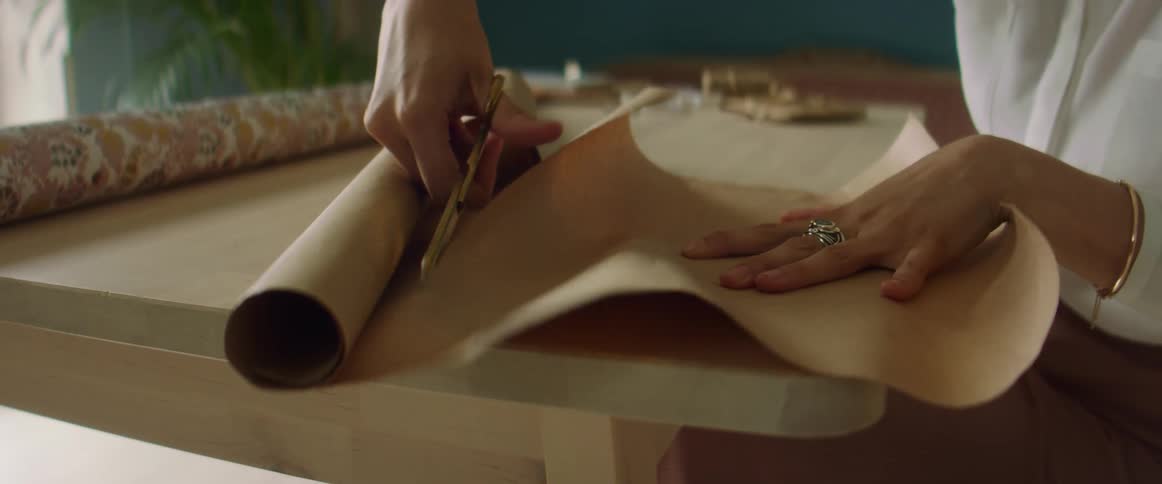 Young blonde fashion designer cutting paper for a pattern over a desk on her studio