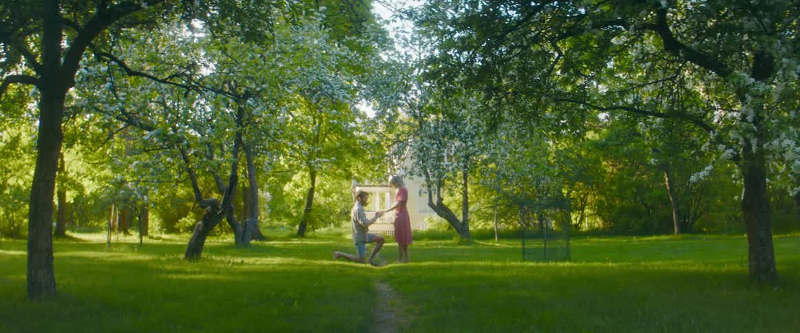 A man kneels to propose to a woman before the placing a ring on her finger and rising to embrace her