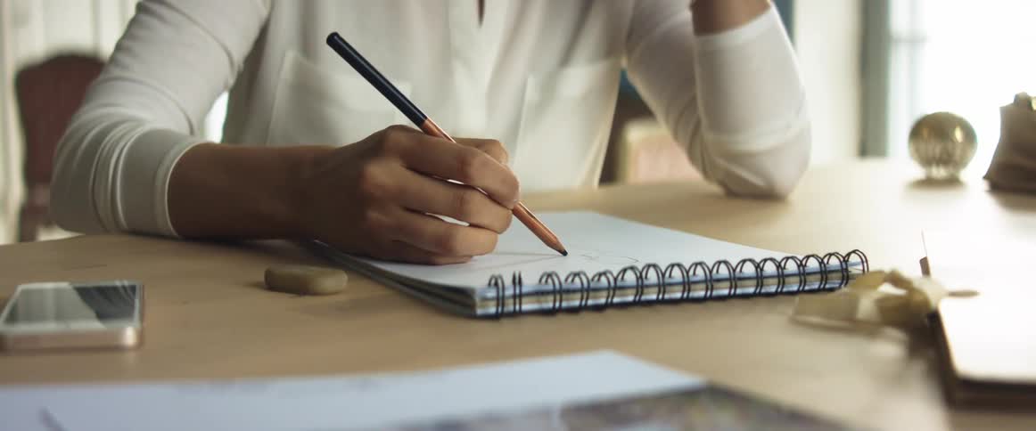 A woman sits at a desk and sketches