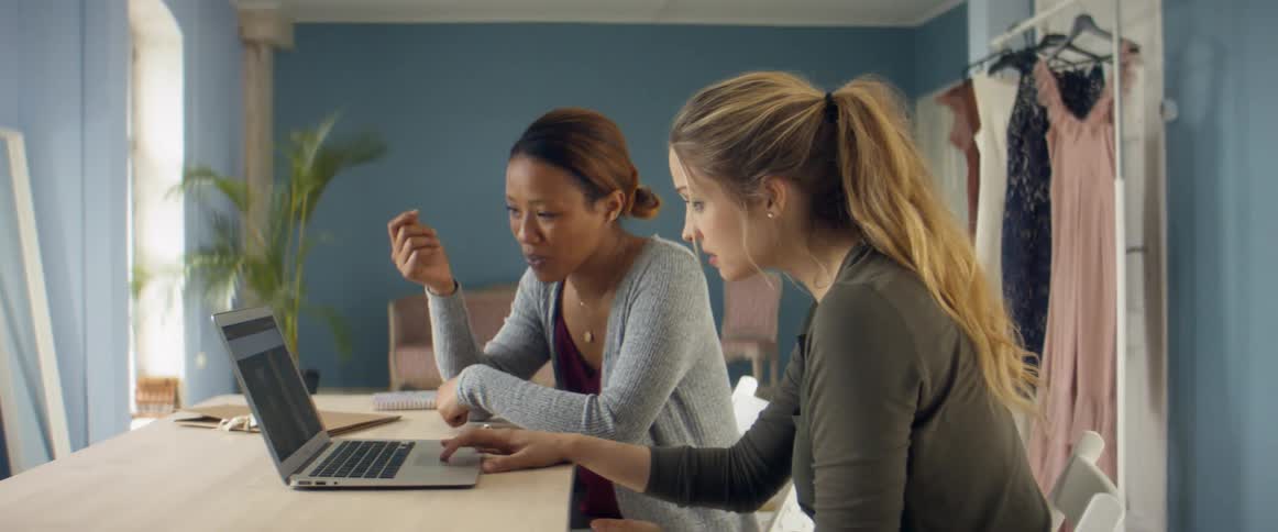 Two women talk and look at a laptop together