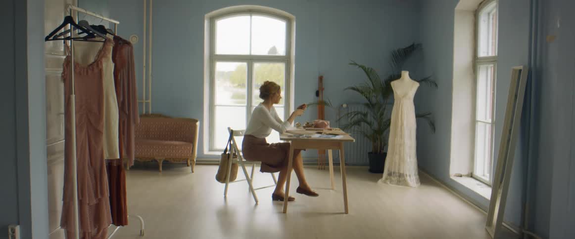 A woman sitting at a desk picks up her phone and looks at it