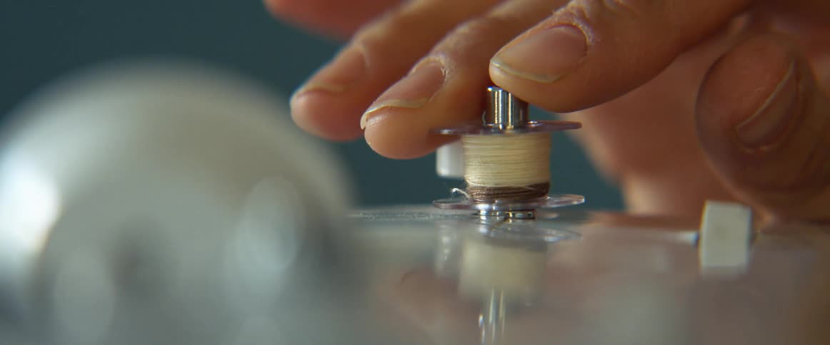 A person in a room placing a roll of thread on a sewing machine