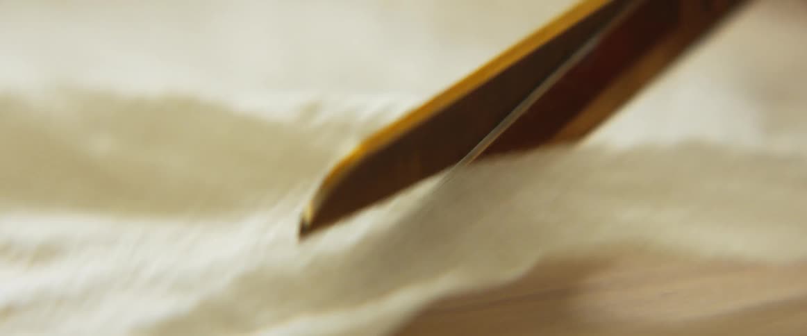A scissor is cutting through a thin cloth