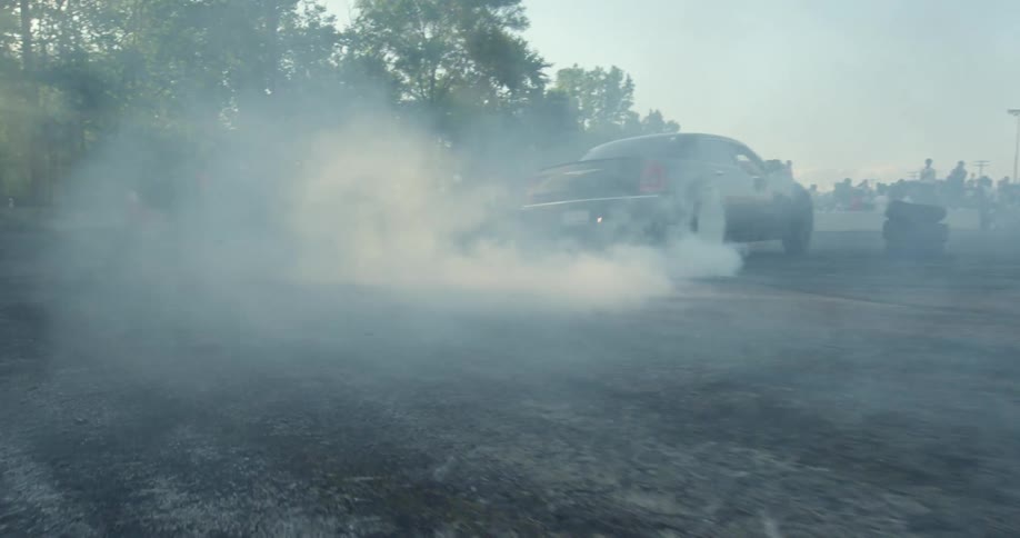 Car burning rubber drifting on a race track in front of a crowd at evening
