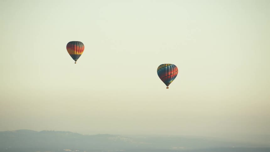 A pair of hot air balloons float through the sky during the day