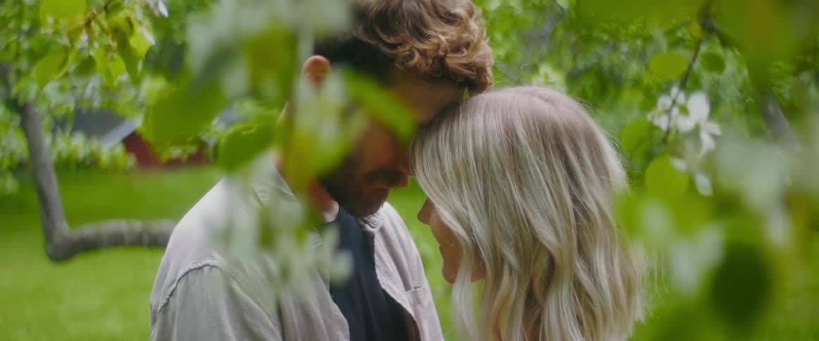 Young couple lovingly embrace touching foreheads under the white flowers hanging from a tree