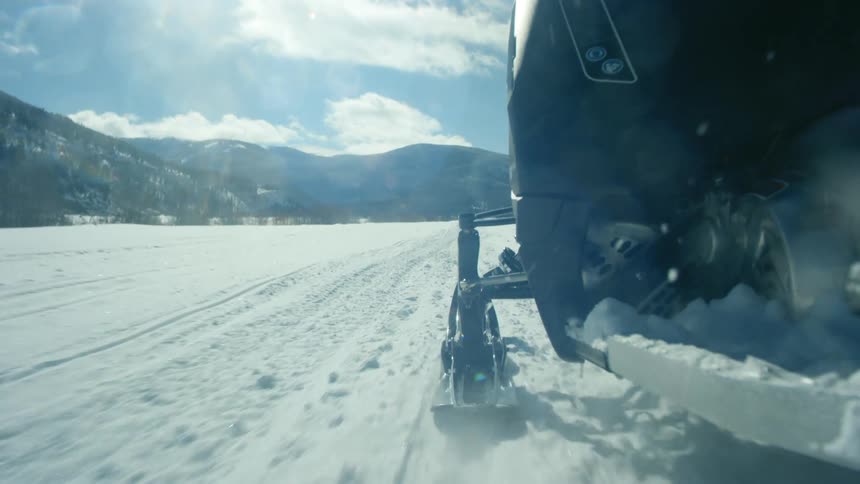 Side view of a snowmobile ski running on snow with mountains visible at a distance