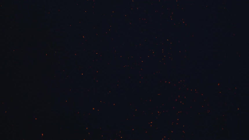 Sparks from a bonfire floating up to the sky at night