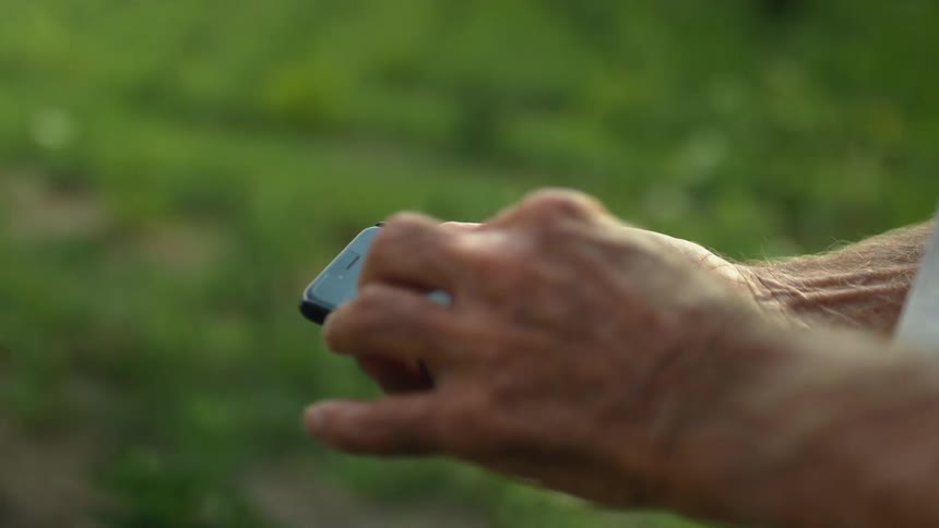 A man using a smart phone with a grassy field in the background