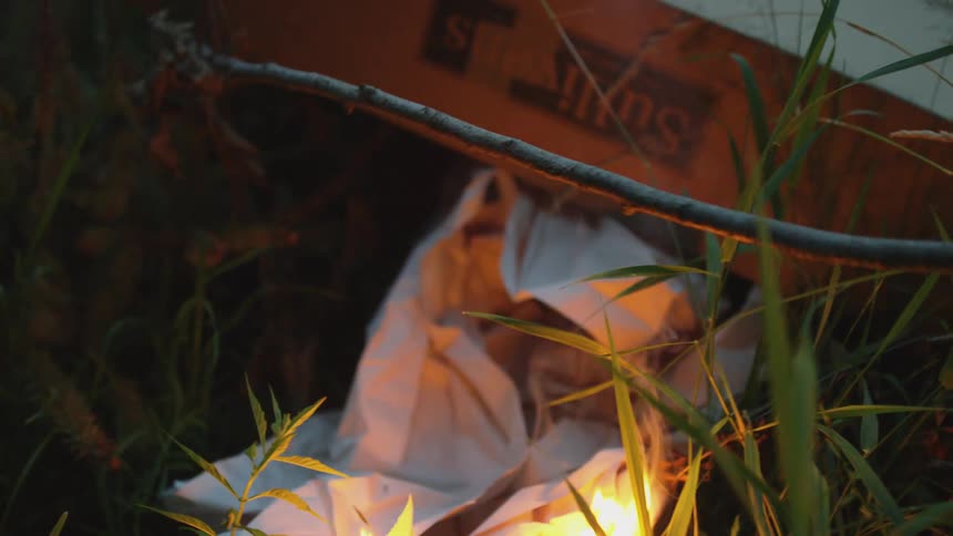 A person with a match setting a piece of paper on fire with smoke