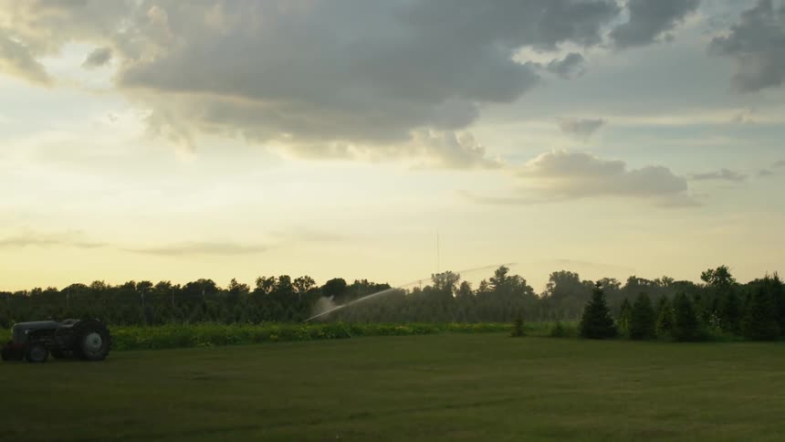 A tractor sits on farmland as a sprinkler waters the grass