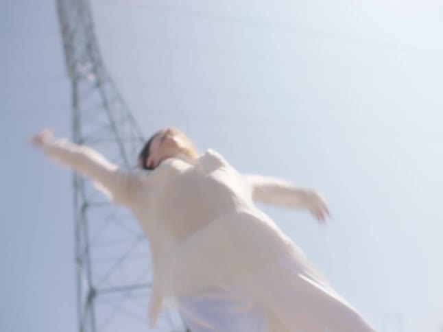 A woman dancing on a road with an antenna the sky and clouds in the background