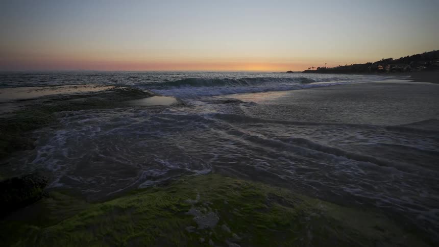 The tide washes into a beach at sunset
