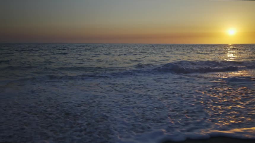 A beach with sand with the ocean a sunset the sky and clouds in the background