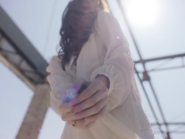 A woman dances outside in a pergola in a sheer white blouse