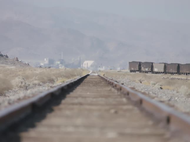 Empty train tracks with a train on different tracks to the side and a town and mountains in the background