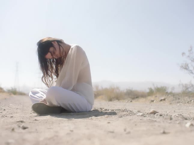 A woman sits alone on a quiet beach and hangs her head