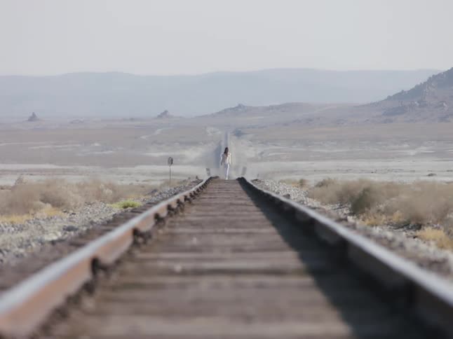 Young woman wearing white clothes walking on the train tracks in the desert
