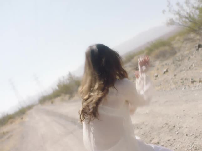 Young woman wearing white clothes dancing on a dirt road in the desert