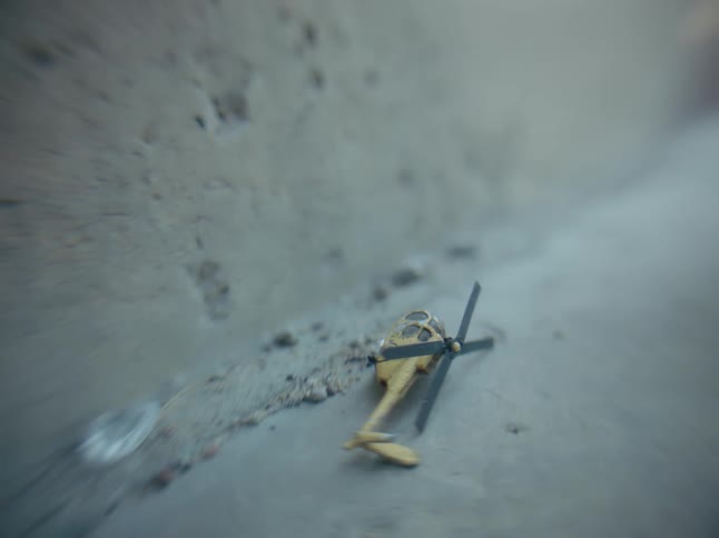 A toy helicopter lies in the soil