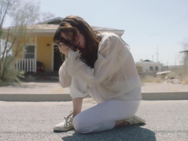 A woman kneeling in the street rubs her hands through her hair